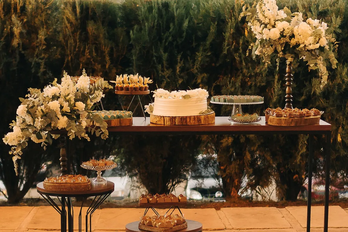 Outdoor wedding dessert table with a white cake, assorted sweets and floral arrangements