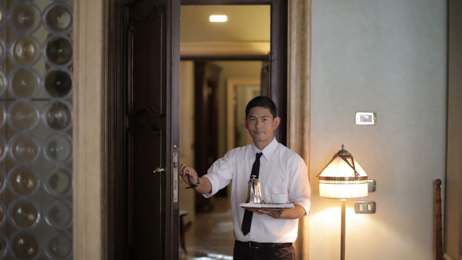Server carrying a tray with coffee through a warmly lit doorway