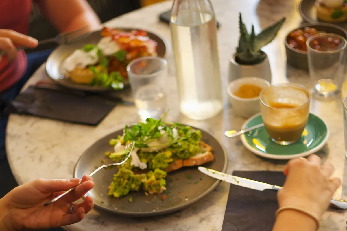 Diners sharing avocado toast, salad and coffee around a café table