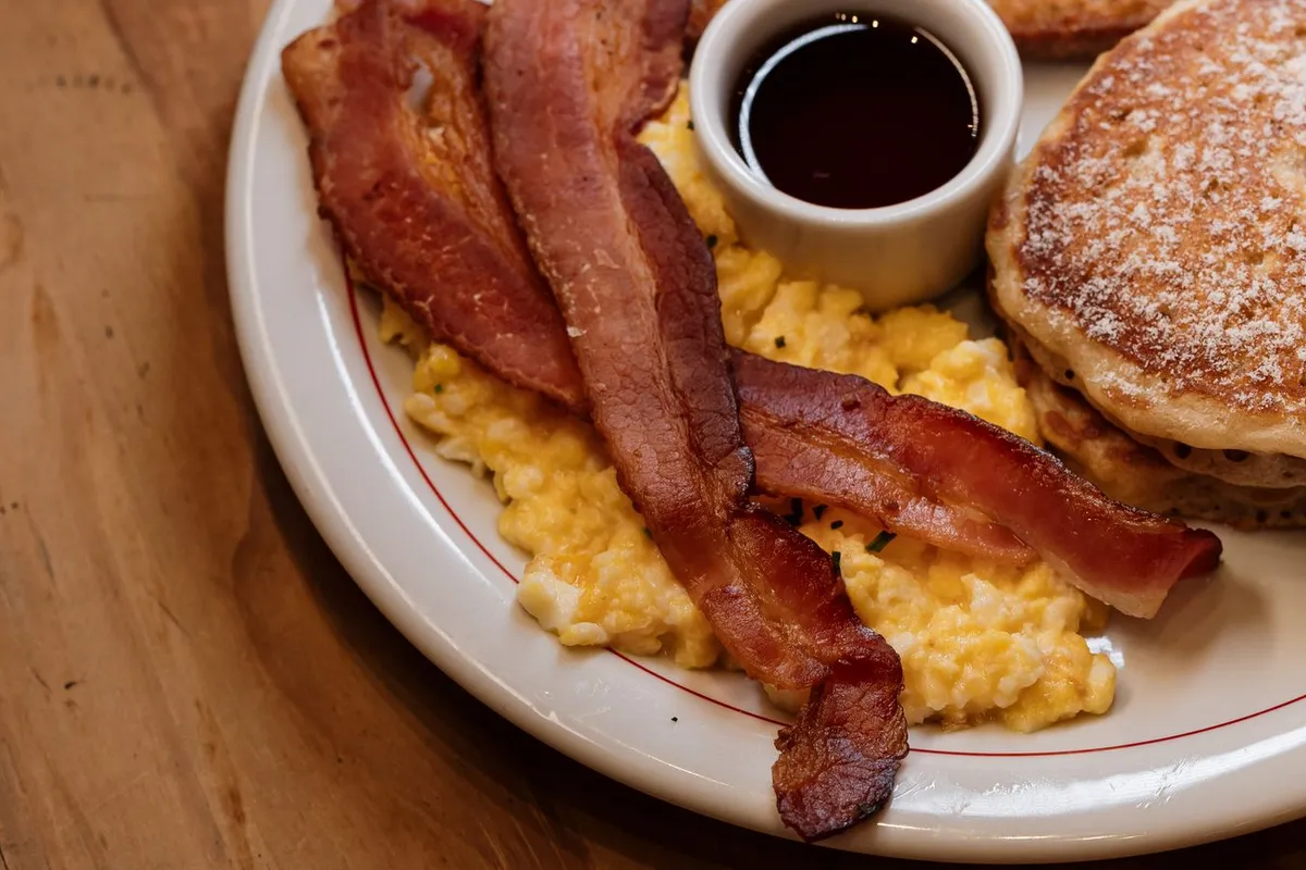Breakfast plate with pancakes, bacon, scrambled eggs, toast and syrup