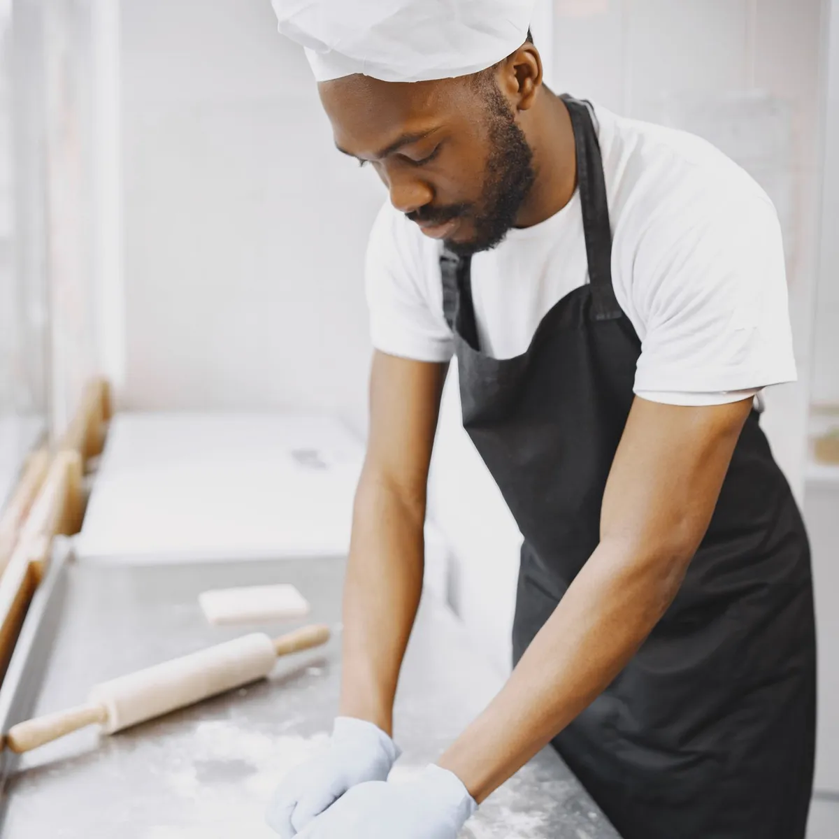 Baker wearing a white hat and black apron kneading dough on a floured work surface