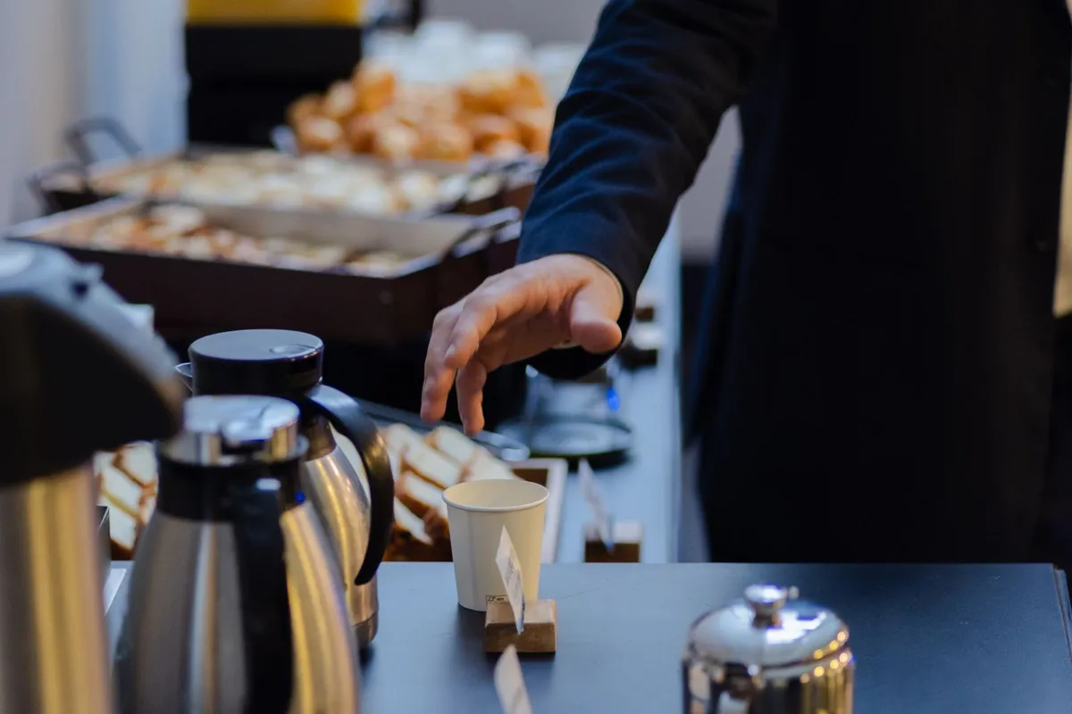 Guest reaching for a cup at a breakfast buffet with coffee carafes, juice and pastries