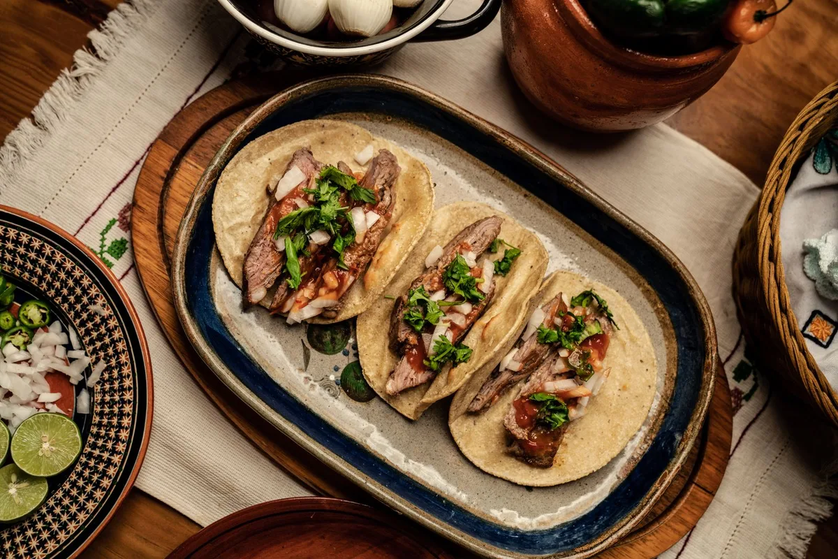 Three steak tacos on tortillas topped with chopped onion and cilantro