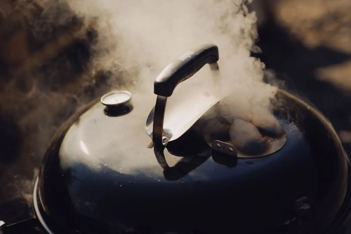 Smoke rising from the lid of a kettle barbecue grill outdoors